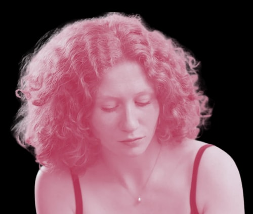 Portrait d'une femme aux cheveux longs et bouclés, au regard sérieux, teintée d'une nuance rosée, avec un fond transparent.