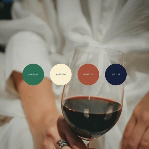 Une main tenant un verre de vin rouge avec des échantillons de couleurs en bas, incluant un vert, une couleur crème, un rouge et un brun.