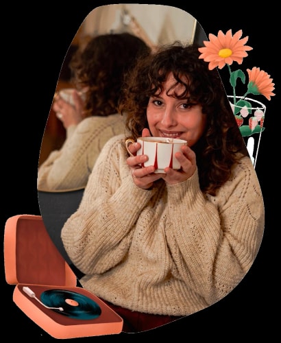 Femme souriante tenant une tasse de café, portant un pull en laine, avec un phonographe et des fleurs en arrière-plan.