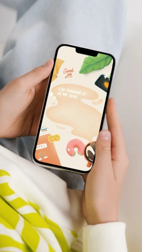 Une personne tient un smartphone affichant un écran décoratif avec des éléments graphiques colorés, comprenant des fleurs, des fruits, et du texte qui dit 'J'ai terminé et je me sens'.