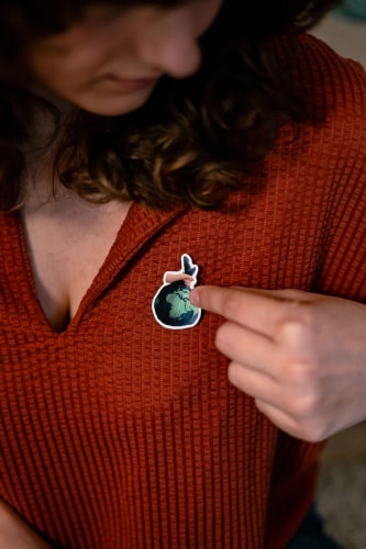 Femme en pull rouge pointant un autocollant représentant une plante sur son vêtement.