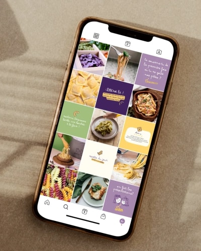 Un téléphone portable affichant une grille de photos de plats de pâtes et des citations culinaires sur un fond beige.