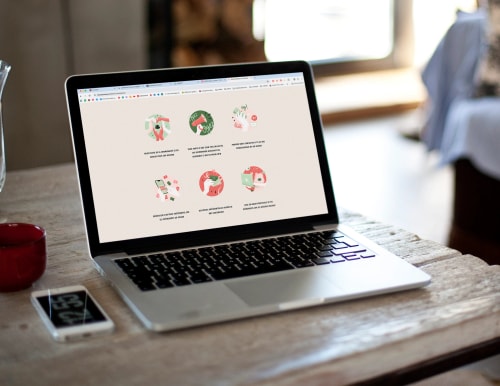 Ordinateur portable sur une table en bois affichant des illustrations sur un fond clair, avec un téléphone à côté.