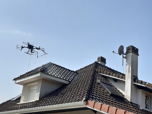 Drone en cours d'intervention de démoussage de toiture.