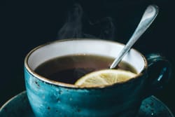 Tasse de thé fumant avec une rondelle de citron, posée sur une soucoupe, avec une cuillère en métal à l'intérieur.