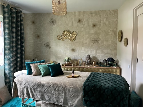 Salon de massage Abracadabra Spa, situé à Wasquehal, Nord. Chambre de spa avec un lit de massage, des coussins verts et une décoration murale élégante, comprenant des éléments dorés et une ambiance apaisante.