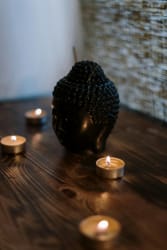 Une statue de Bouddha noire en céramique avec des bougies allumées autour, posée sur une table en bois.
