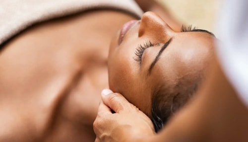 Femme allongée avec les yeux fermés, recevant un massage au niveau de la tête, un soin apaisant avec une main posée sur son épaule.
