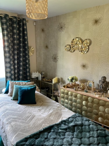 Vue intérieure du salon de massage Abracadabra Spa, situé à Wasquehal à travers une fenêtre, avec des murs en briques et des décorations murales. Le lit est recouvert d'une couette verte, des plantes en pot sont placées sur le rebord de la fenêtre.