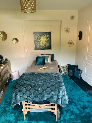 Chambre décorée avec un lit simple, des coussins et un plaid bleu-vert, des murs beige, et des décorations murales dorées et vertes.