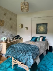 Salon de massage Abracadabra Spa, situé à Wasquehal, Nord. Chambre de spa élégante avec un lit de massage recouvert d'une couverture douce, décorée de coussins turquoise et d'une œuvre d'art dorée sur le mur.