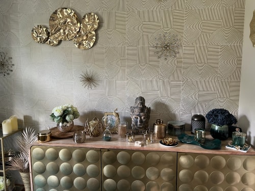 Salon de massage Abracadabra Spa, situé à Wasquehal, Nord. Une décoration intérieure avec une commode dorée, ornée de divers objets décoratifs tels que des vases, des statues et des plantes, contre un mur texturé avec des motifs géométriques.