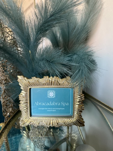 Salon de massage Abracadabra Spa, situé à Wasquehal, Nord. Une petite plaque décorative en or sur une table, affichant le nom 'Abracadabra Spa' et un logo, entourée de feuillages décoratifs.