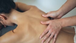 Une personne recevant un massage sur le dos, avec une vue rapprochée des mains du masseur en train de masser la peau exposée.