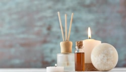 Une composition de produits de bien-être comprenant des bâtonnets de diffusion, une bougie allumée, une bouteille d'huile essentielle et une boule de savon, sur un fond flou.