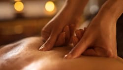Deux mains effectuant un massage sur le dos d'une personne, avec des bougies floues en arrière-plan.
