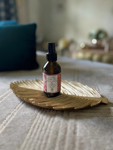 Bouteille d'huile biologique sur un plateau en forme de feuille, posée sur une surface douce et texturée.