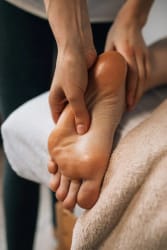 Une personne effectue un massage des pieds, avec une serviette beige en dessous.