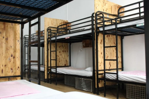 Dortoir avec plusieurs lits superposés à structure métallique noire, matelas blancs et murs en bois clair.