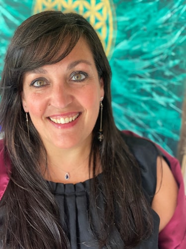 Portrait de Sandra ROUSSEAU, souriante avec des cheveux longs et noirs, portant un haut noir et des boucles d'oreilles pendantes, devant un arrière-plan coloré avec un motif géométrique.