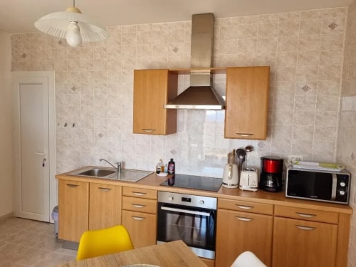 Cuisine moderne avec des armoires en bois, un évier, une cuisinière, un four, un réfrigérateur et un micro-ondes, avec une table à manger jaune.