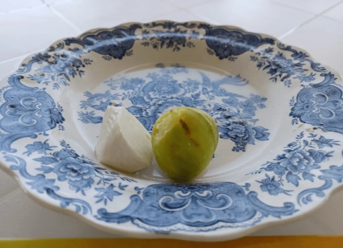 Une assiette en porcelaine bleue avec un morceau de fromage blanc et une figue verte.