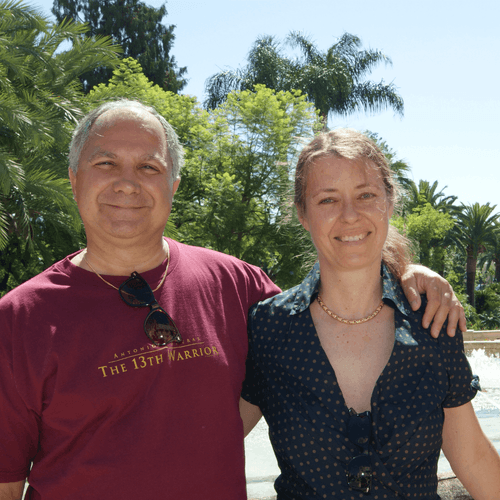 Alain et Florence se tenant côte à côte dans le jardin de leur maison, avec des palmiers et de la verdure en arrière-plan.