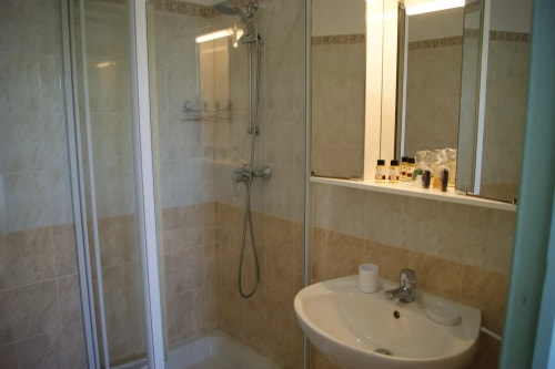 Salle de bain avec douche vitrée, lavabo et armoire murale, décoration en carrelage beige.