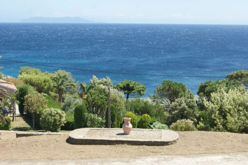 Vue panoramique d'un paysage côtier avec un pot en terre cuite au premier plan, entouré de verdure et avec la mer bleue à l'arrière-plan.