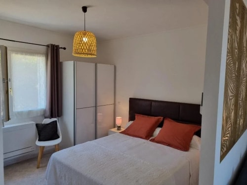 Chambre à coucher avec un lit double, des oreillers orange, une lampe de chevet, des rideaux et un meuble de rangement blanc.