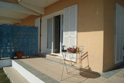 Terrasse d'une maison avec un écran bleu, une table pliante et un panier sur le dessus, et une porte-fenêtre donnant à l'intérieur.