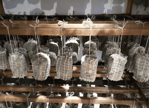 Des morceaux de viande suspendus dans des filets sur des étagères en bois, dans un environnement de salaison.