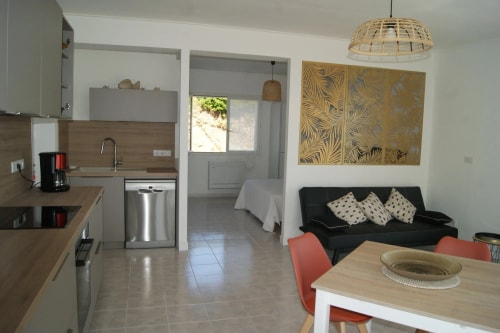 Une vue intérieure d'un appartement moderne avec une cuisine équipée, un coin salon avec un canapé, et une table à manger. Il y a des décorations murales dorées et de la lumière naturelle qui entre par une fenêtre.