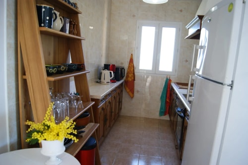 Une cuisine bien équipée avec des étagères en bois, des appareils électroménagers, des pots et des ustensiles de cuisine, ainsi qu'une fenêtre laissant entrer la lumière naturelle.