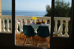 Table de terrasse avec des chaises, décorée de fleurs et d'aliments, donnant sur une vue de la mer.