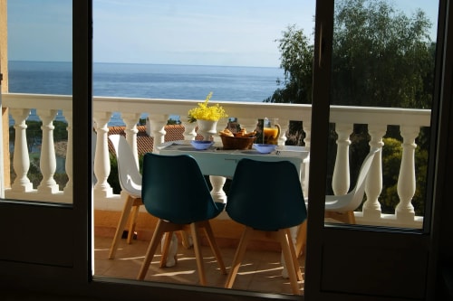 Table de terrasse avec des chaises, décorée de fleurs et d'aliments, donnant sur une vue de la mer.