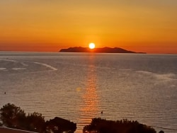 Coucher de soleil sur une mer calme, avec une île silhouette à l'horizon et des couleurs orange et dorées dans le ciel.