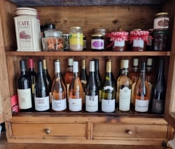 Une étagère en bois remplie de différentes bouteilles de vin et de confitures, avec des bocaux et un contenant de café en haut.