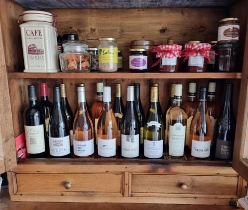 Une étagère en bois remplie de différentes bouteilles de vin et de confitures, avec des bocaux et un contenant de café en haut.