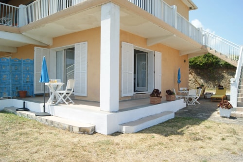 Maison A Pianatella à deux étages avec balcons, escalier et chaises longues devant, sous un ciel bleu.