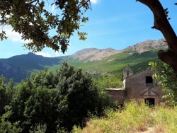 Vue d'un paysage montagneux avec une maison en ruine entourée de verdure et d'arbres.