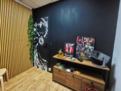 Salon avec mur noir décoré d’affiches et de plantes, meuble TV en bois avec écran, figurines et objets décoratifs, parquet clair et panneau mural en bois.