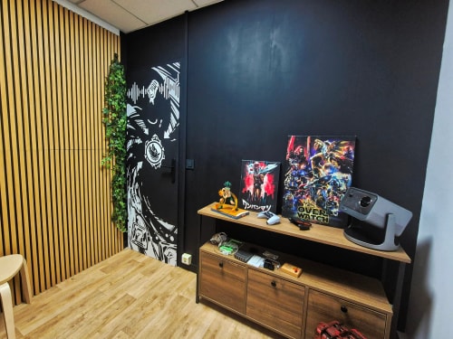 Salon avec mur noir décoré d’affiches et de plantes, meuble TV en bois avec écran, figurines et objets décoratifs, parquet clair et panneau mural en bois.