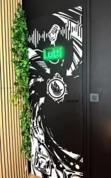 Porte noire ornée de motifs graphiques blancs, bordée de plantes grimpantes, dans un intérieur au sol en bois.