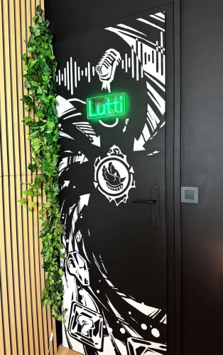 Porte noire ornée de motifs graphiques blancs, bordée de plantes grimpantes, dans un intérieur au sol en bois.