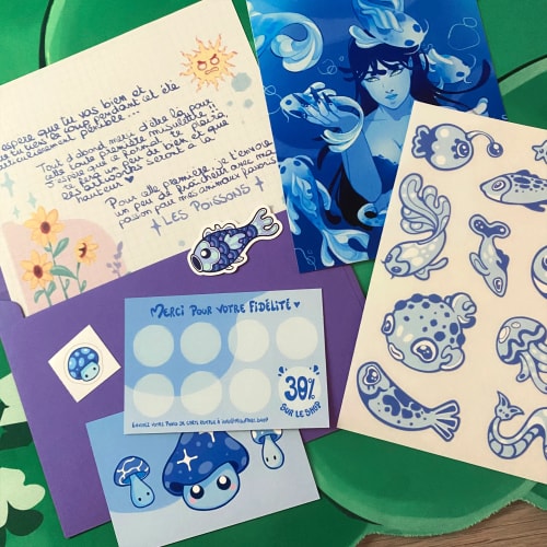 Cartes et illustrations colorées sur un support vert : dessin marin bleu, motifs de poissons, message manuscrit, autocollants et palette pastel.