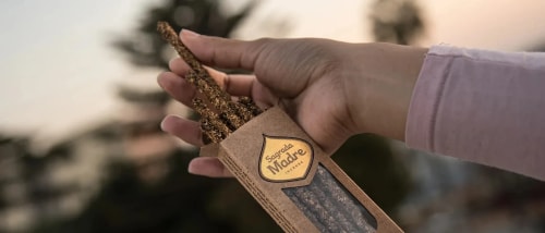 Main tenant une boîte en carton ouverte contenant des bâtons d'encens étiquetés «Sagrada Madre Incense» avec un fond flou extérieur en fin de journée.