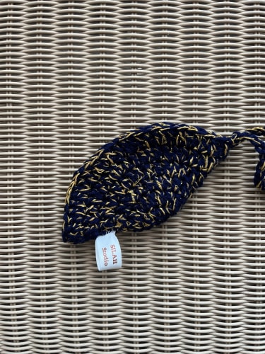 Petit sac à main crocheté avec un motif bicolore en bleu nuit et blanc, doté d'une longue bandoulière assortie, posé sur un sol carrelé beige.