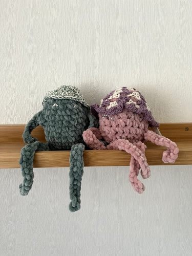 Petit sac à main crocheté avec un motif bicolore en bleu nuit et blanc, doté d'une longue bandoulière assortie, posé sur un sol carrelé beige.