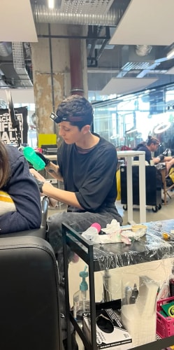 Tatoueuse portant une lampe frontale, travaillant dans un studio professionnel avec du matériel médical, une cliente assise devant elle et un chariot contenant des fournitures de tatouage au premier plan.